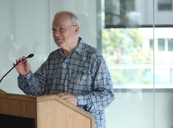 King stands behind a podium and adjusts the podium microphone while addressing an unseen audience.