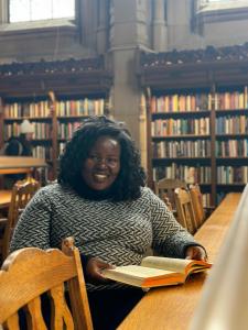 PhD student Cynthia Auma sitting at a table in the UW library smiling