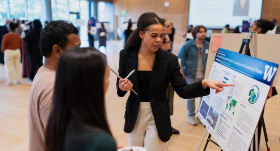 A student presents a research poster at a research event in an auditorium.
