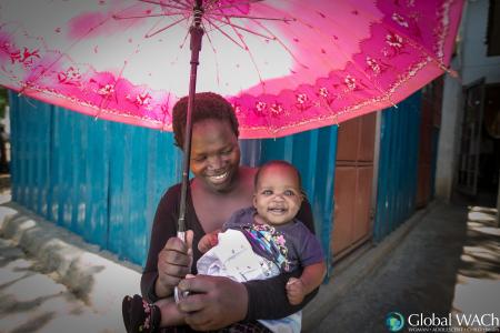 Women standing under an umbrella holding a smiling baby