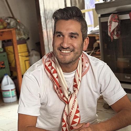 Headshot of Ale Barrientos wearing a white t-shirt and a red and white checkered scarf.