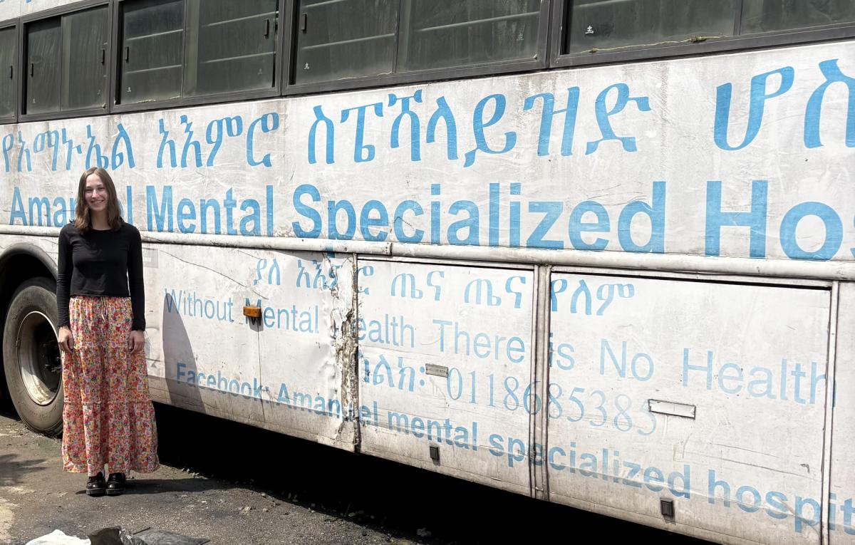 Erickson Brooke standing in front of a white bus with the words "Without Mental Health There is No Health" written in blue on it.