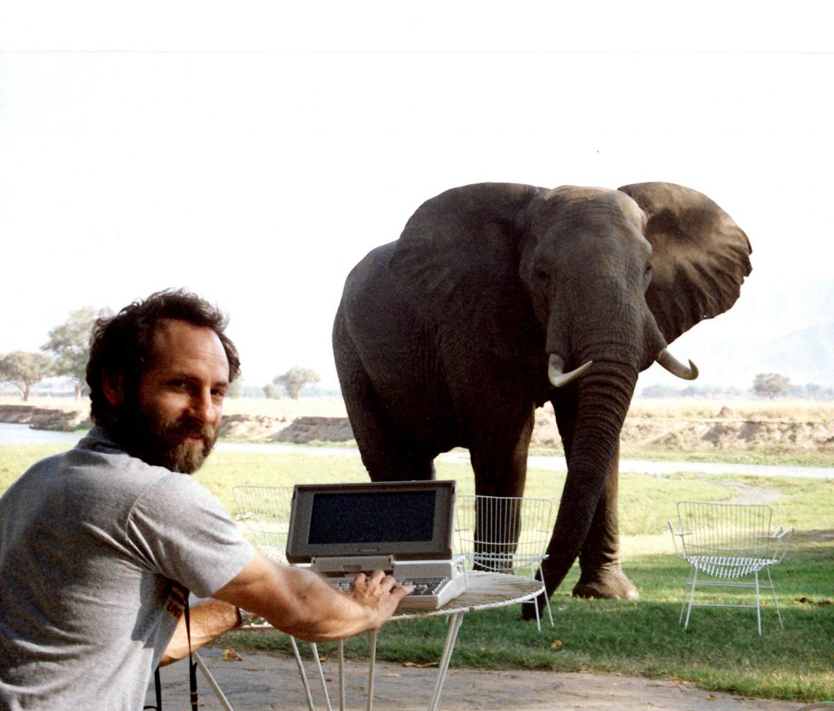 Dr. Jay Kravitz in Lesotho seated at a table with a laptop in front of an elephant. 