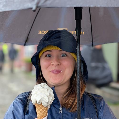 Shelby Thurman wearing a rain jacket, holding an umbrella, and eating ice cream.