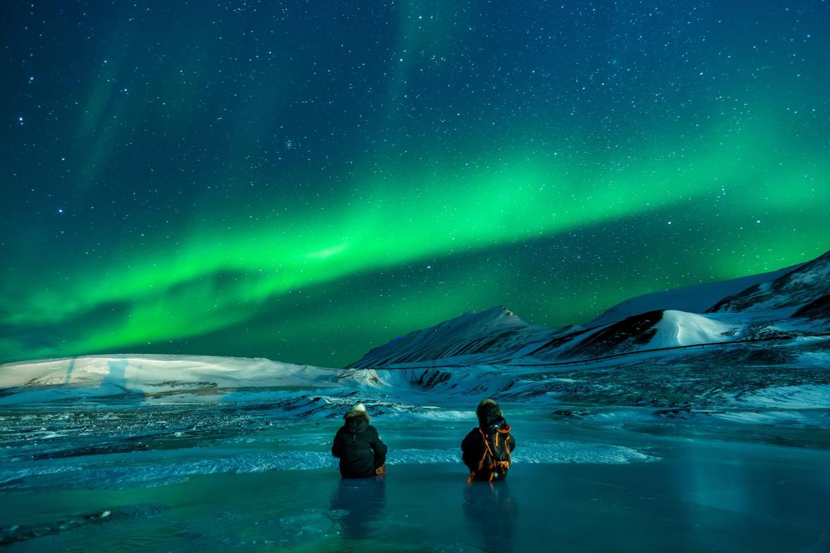Photo of two people sitting under the Northern Lights